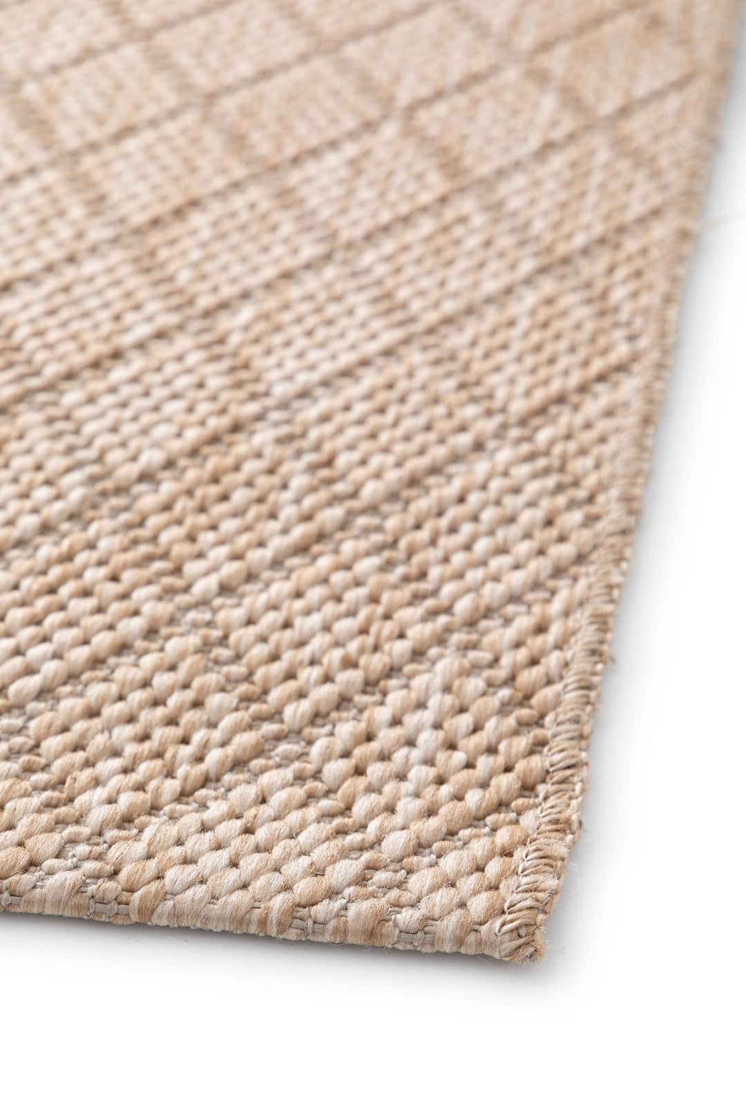 Close-up of beige woven rug with diamond lattice, stitched corner edge, and chunky texture on white.