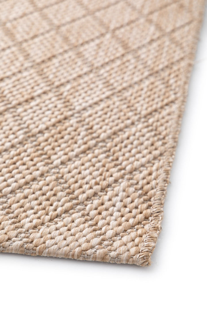 Close-up of beige woven rug with diamond lattice, stitched corner edge, and chunky texture on white.