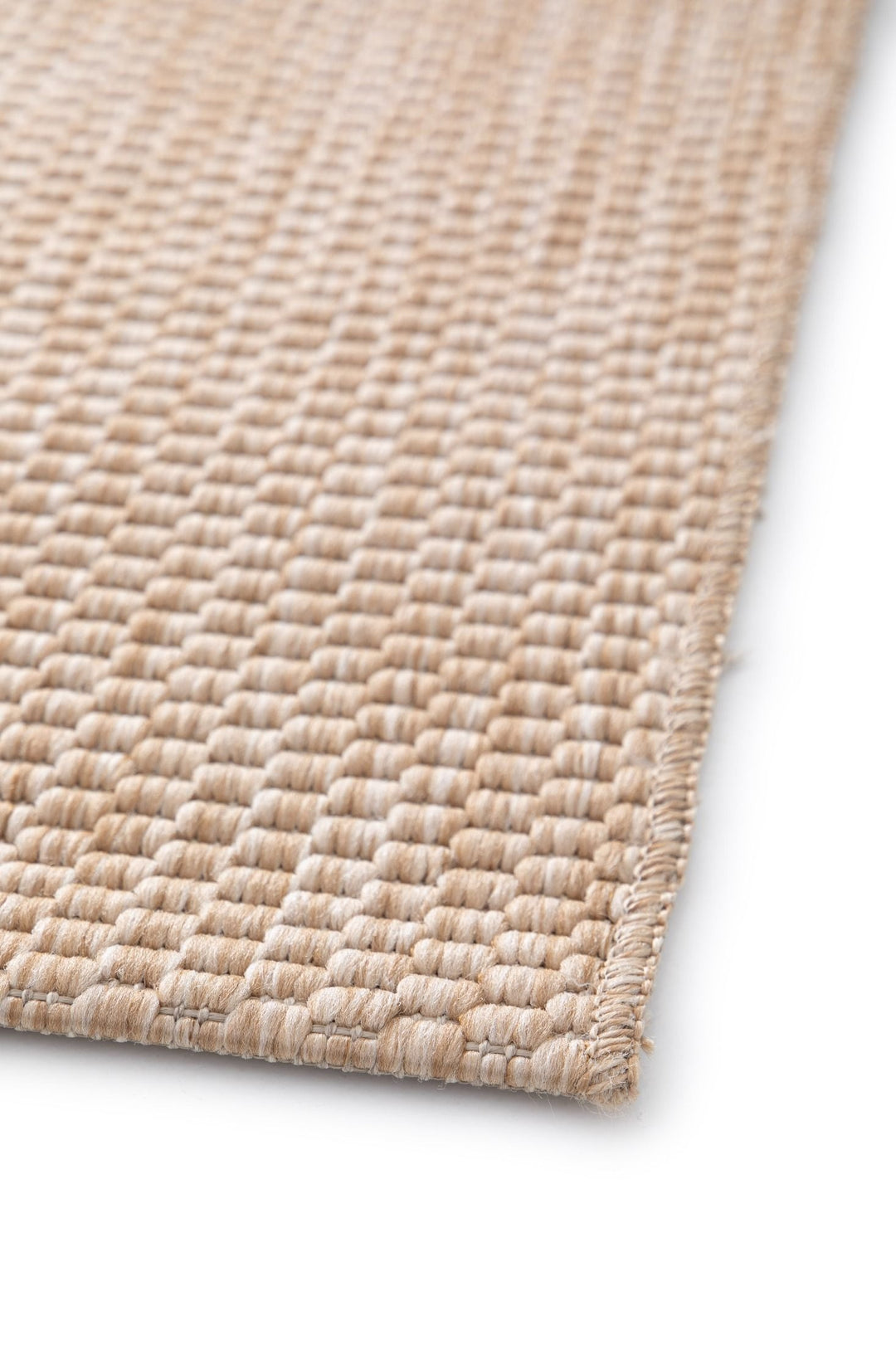 Angled close-up of the Barton indoor/outdoor rug in Sand (41503-070), showing chunky basketweave texture and a neatly serged edge on a white background.