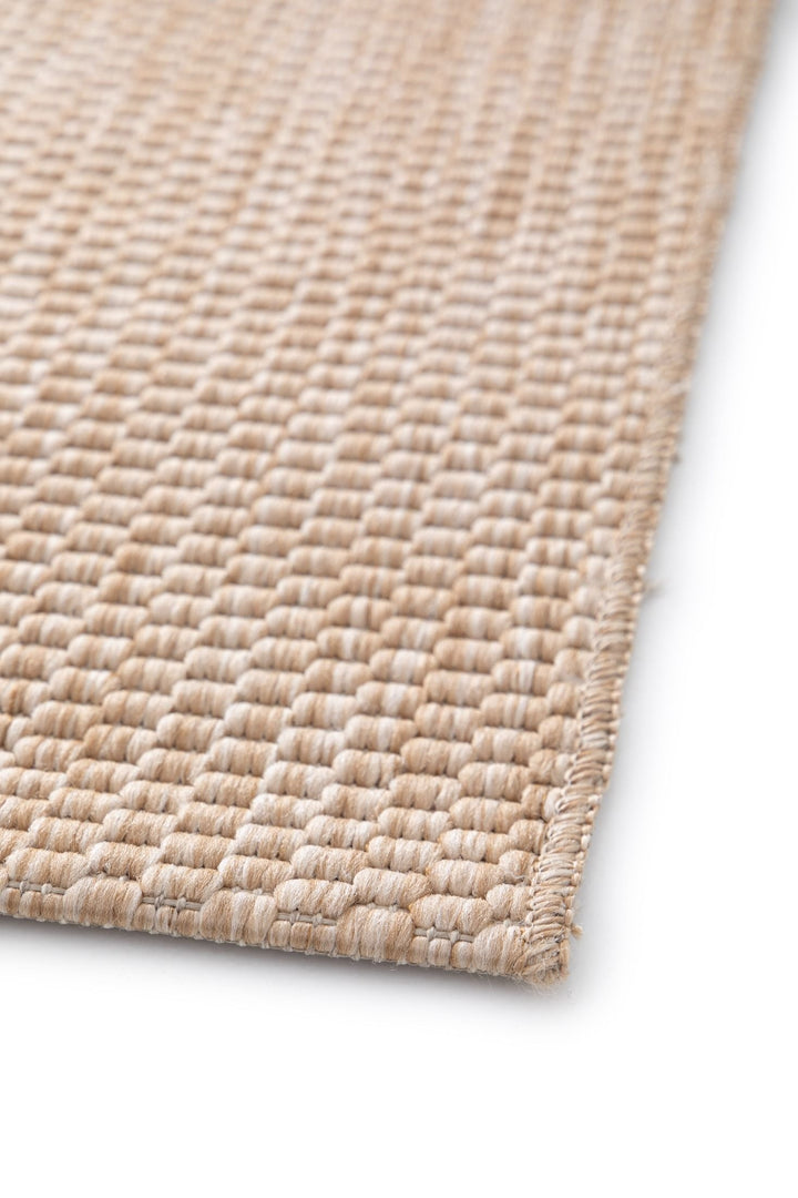 Angled close-up of the Barton indoor/outdoor rug in Sand (41503-070), showing chunky basketweave texture and a neatly serged edge on a white background.