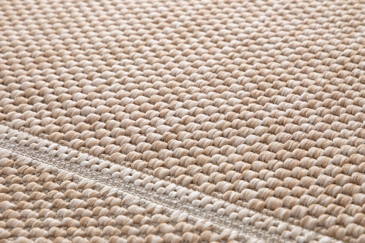 Close-up of a beige woven rug showing chunky looped texture, two-tone fibers, and a stitched seam detail.