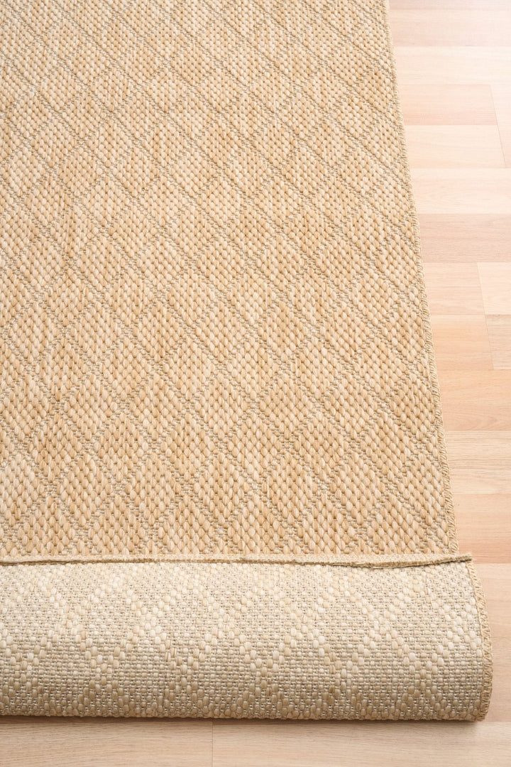 Close-up of tan woven rug with diamond lattice, serged edge, and rolled underside on wood floor.