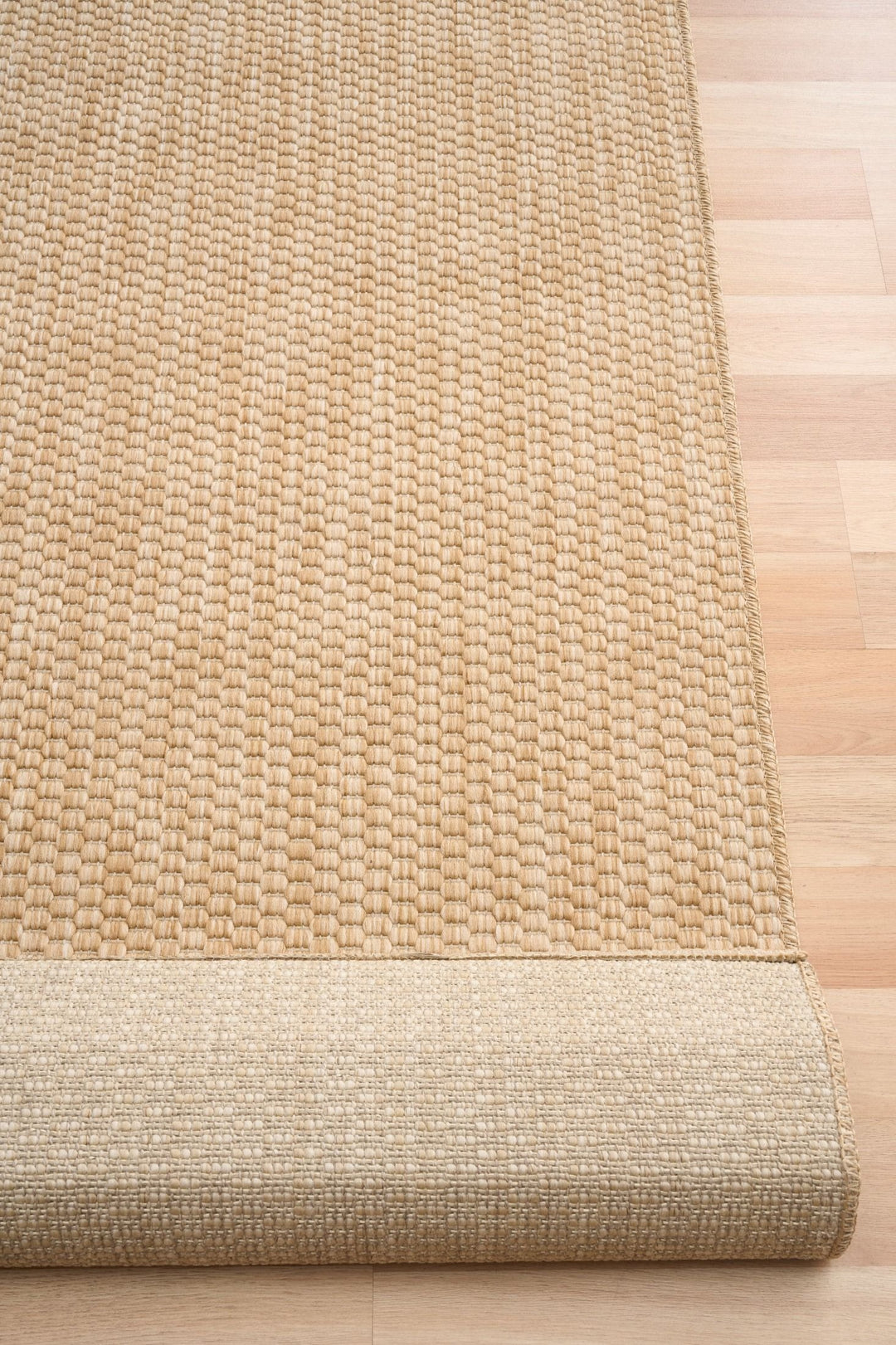 Tan woven rug (Barton 41503/70) rolled edge showing backing, border, and textured weave on light wood floor.