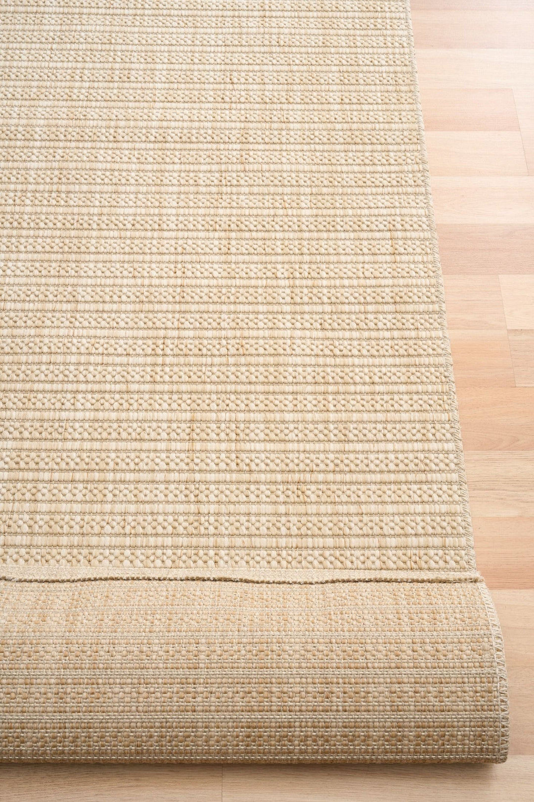 Beige woven rug with raised diamond lattice, rolled corner showing stitched edge and backing.