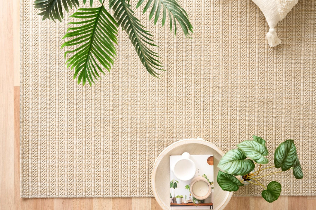Beige ribbed rug on wood floor with palm fronds, throw, and tray.