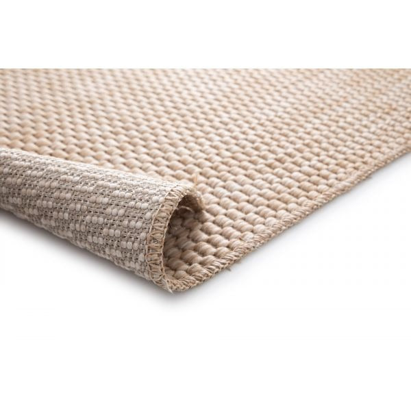 Close-up of the Barton indoor/outdoor flatweave area rug in Sand (41503-070), rolled corner revealing backing, chunky weave, and serged edge on a white background.