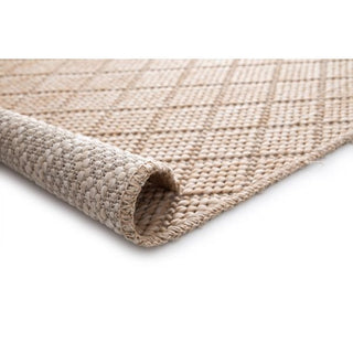Beige woven rug with diamond lattice, rolled corner showing stitched edge and backing in sand/ivory on white.