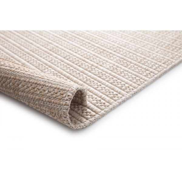 Beige woven rug with diamond pattern, rolled corner showing stitched edge and backing.