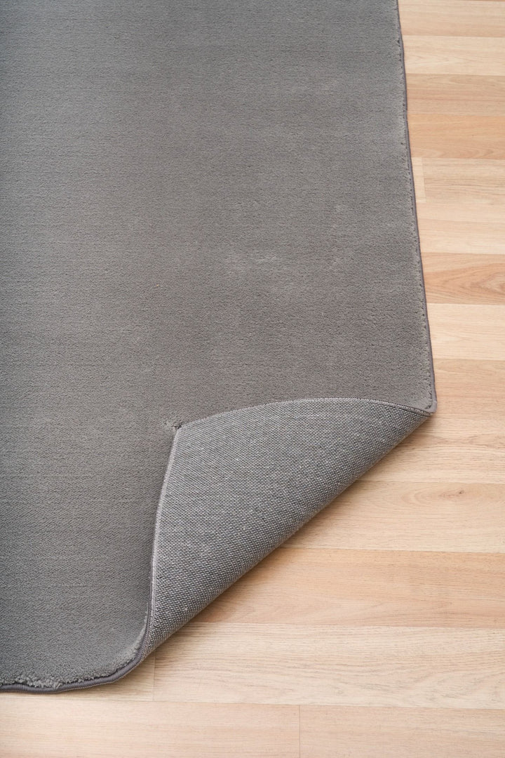 Grey rug corner lifted to reveal its textured underside on a wooden floor.