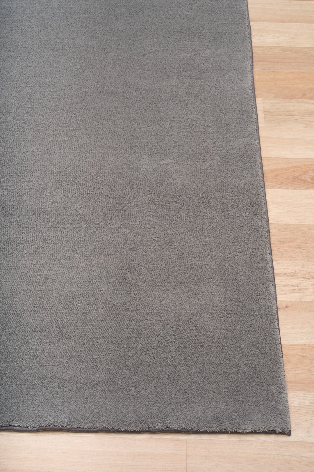 Close-up of a grey rug corner placed on a wooden floor.