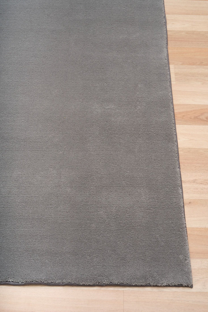 Close-up of a grey rug corner placed on a wooden floor.