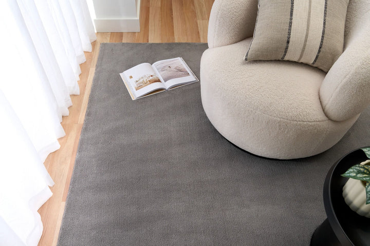 Grey rug in a living room with a cream chair, cushion, and open book.