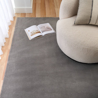 Grey rug under a cream chair and open book in a cozy living room.