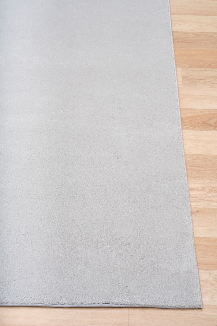 Close-up of a light grey rug corner placed on a wooden floor.