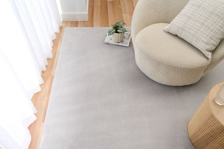 Light grey rug in a modern living room with a cream chair, pillow, and side table.