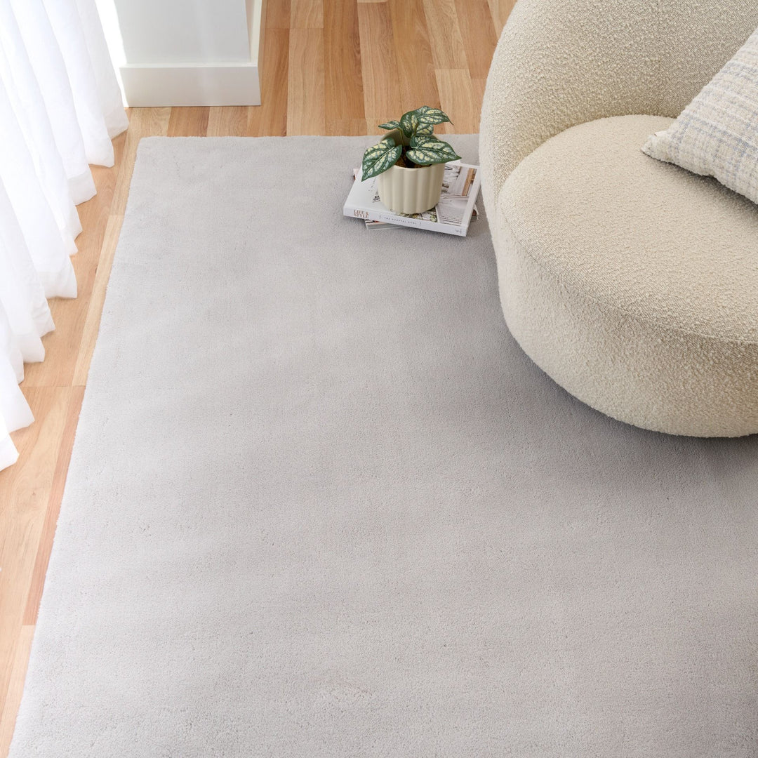Light grey rug under a cream chair with a plaid pillow and small plant nearby.