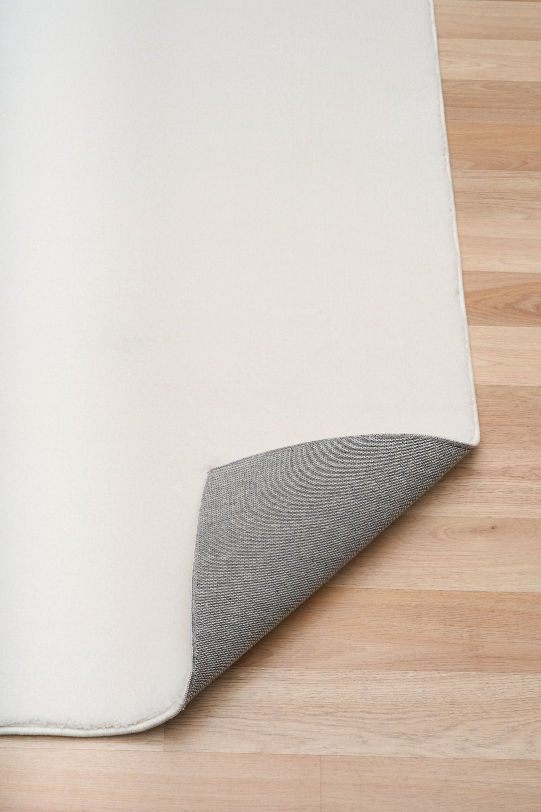 White rug corner lifted to reveal its textured underside on a wooden floor.