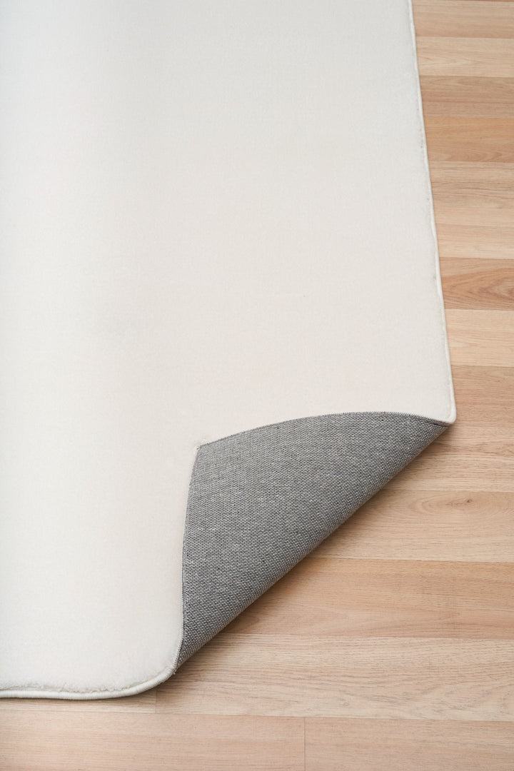 White rug corner lifted to reveal its textured underside on a wooden floor.
