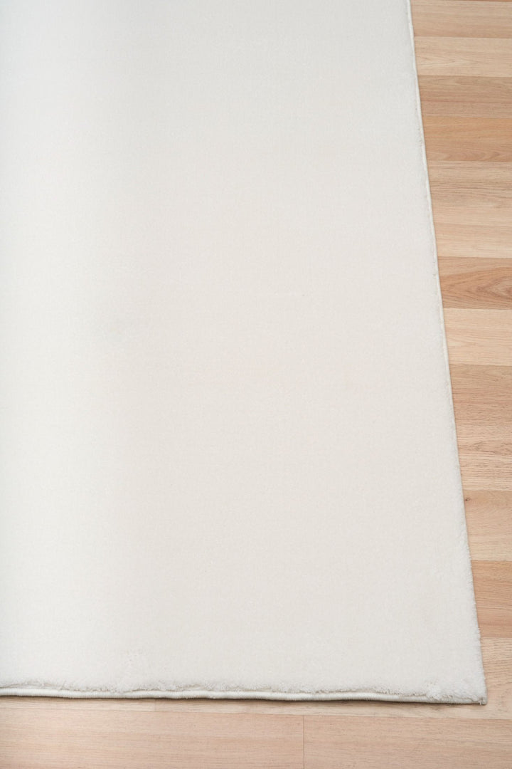 Close-up of a white rug corner placed on a wooden floor.