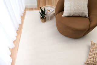 White rug styled in a bright living room with a brown chair and plant basket.