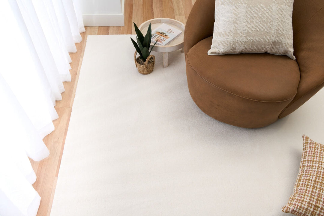 White rug styled in a bright living room with a brown chair and plant basket.