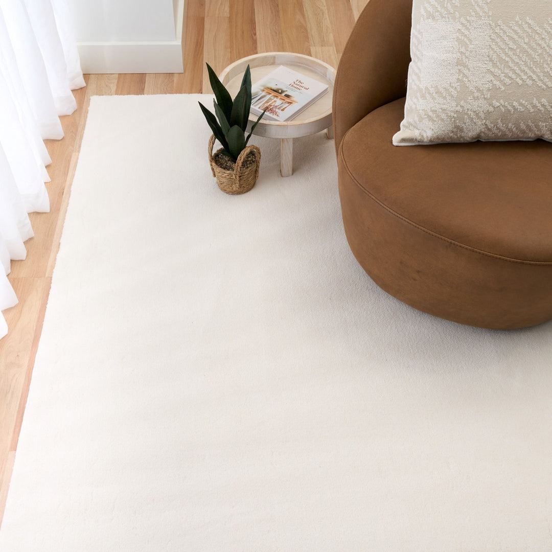 White rug in a modern living room with a brown chair, cushion, and side table.