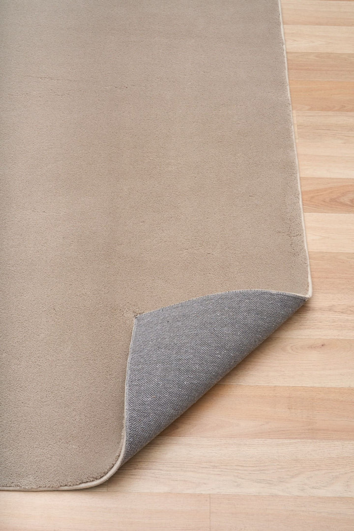 Clay rug corner lifted to reveal its textured underside on a wooden floor.