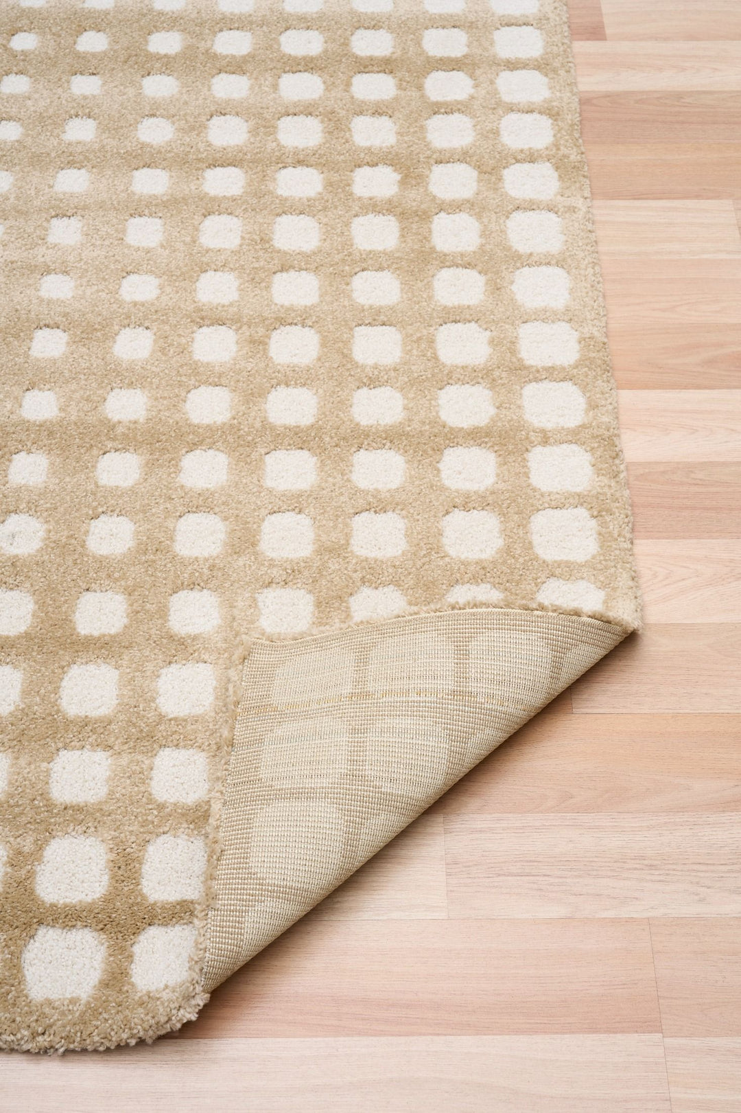 Folded corner of beige rug showing backing.