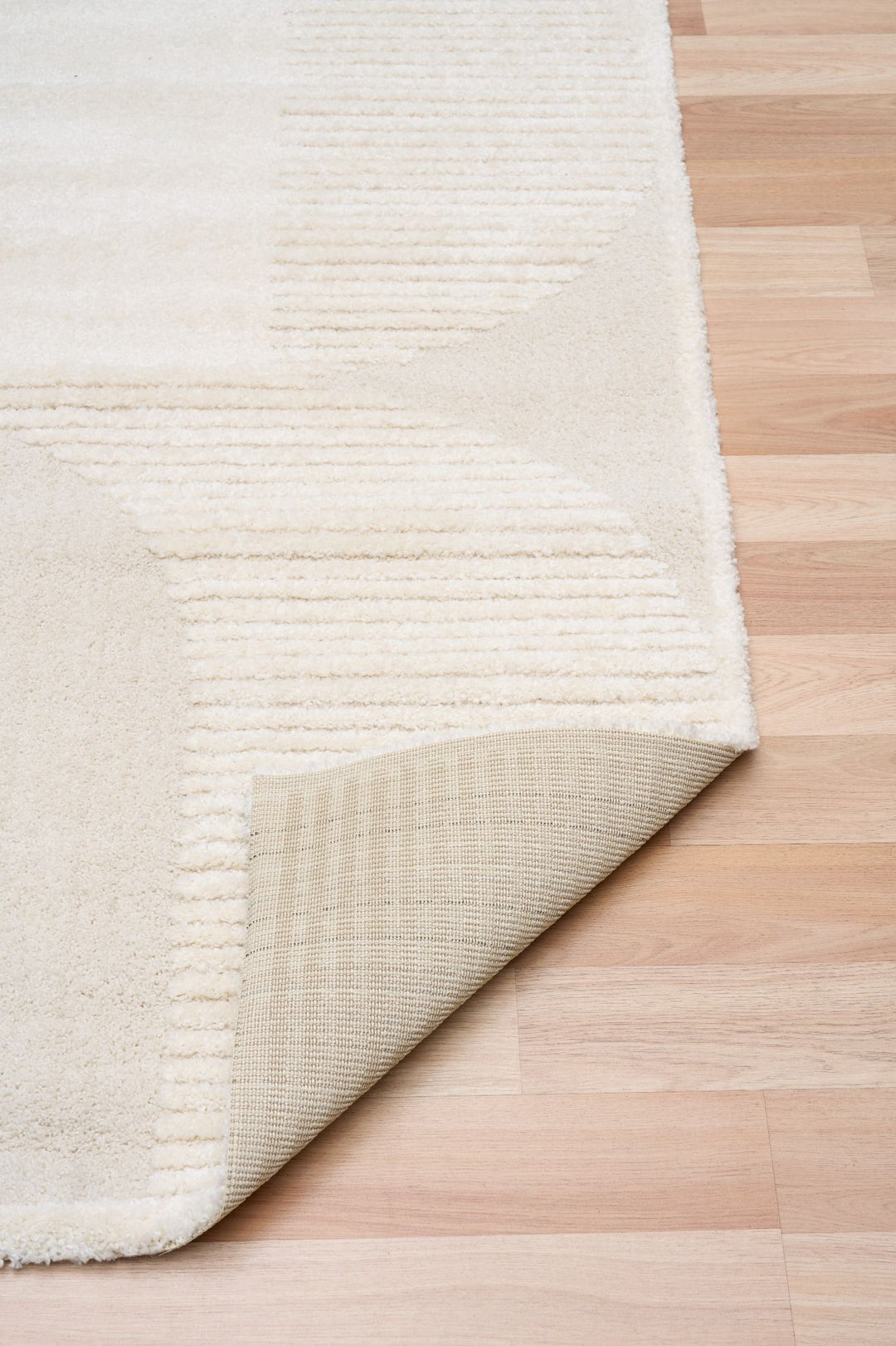 Cream rug corner lifted to show backing detail.