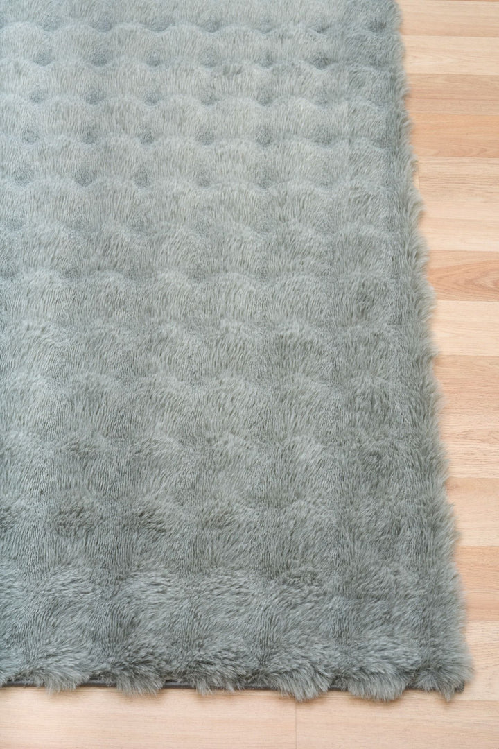 Close-up of green fluffy rug corner on wooden floor.