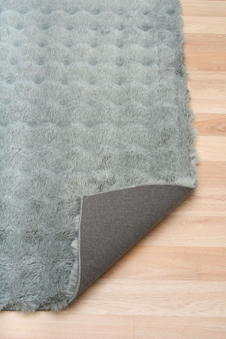 Close-up of green textured rug with corner flipped to show non-slip backing.