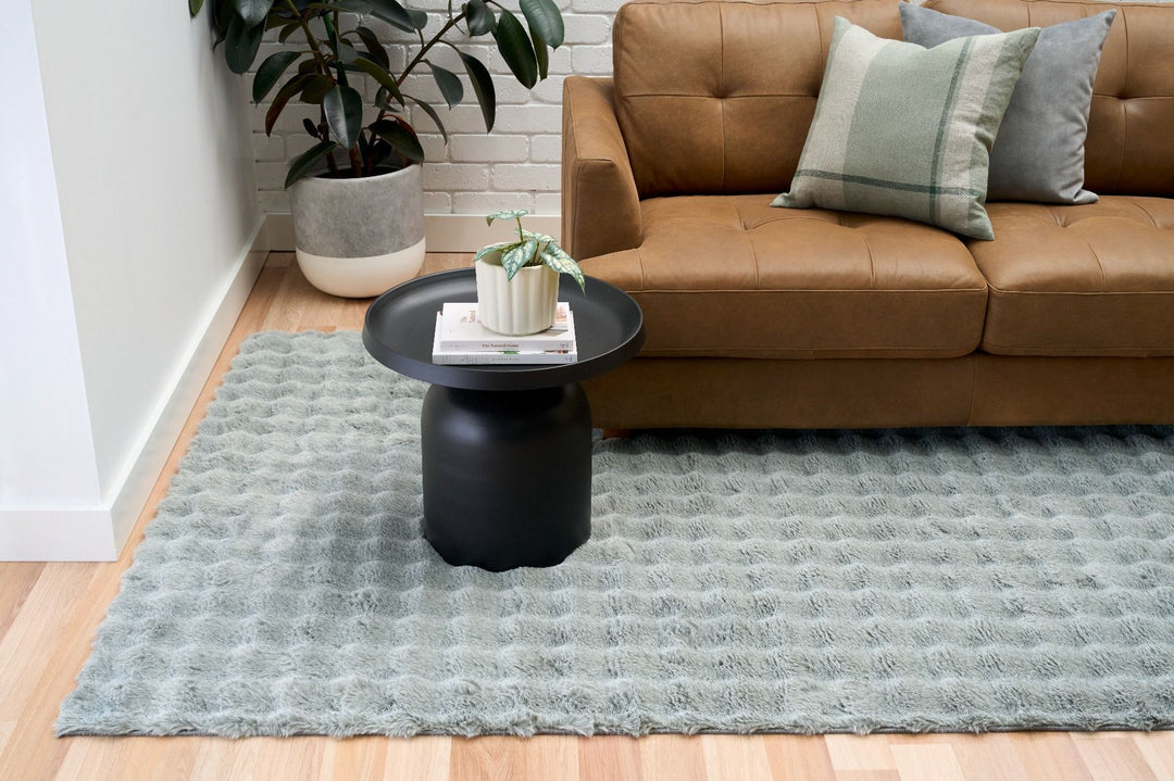Green textured rug in living room with brown leather sofa, pillows, and black round side table.