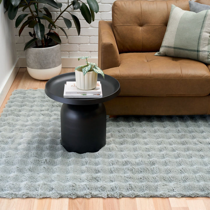 Modern living room with green textured rug, brown leather sofa, and black round side table.