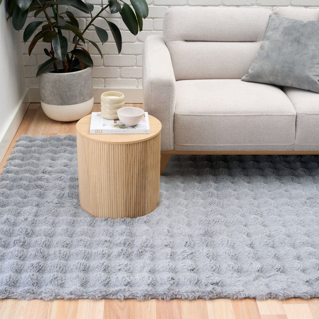Modern living room with grey textured rug, beige sofa, and round wooden side table.