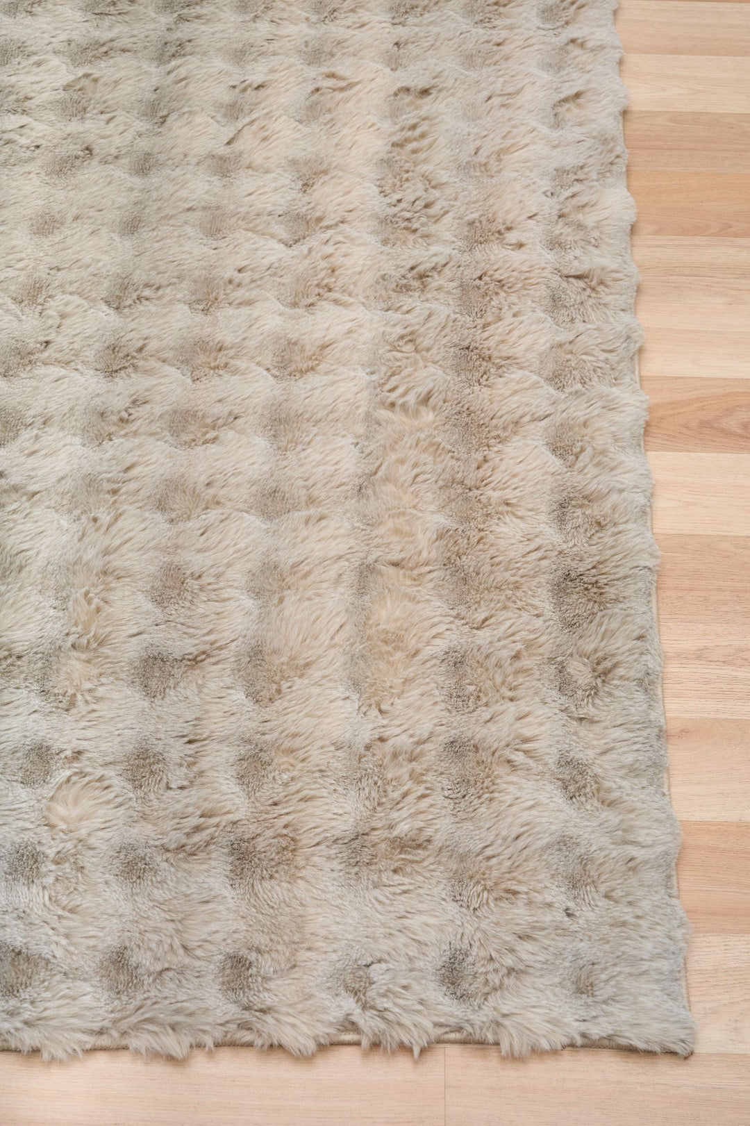 Close-up of light beige fluffy rug corner on wooden floor.