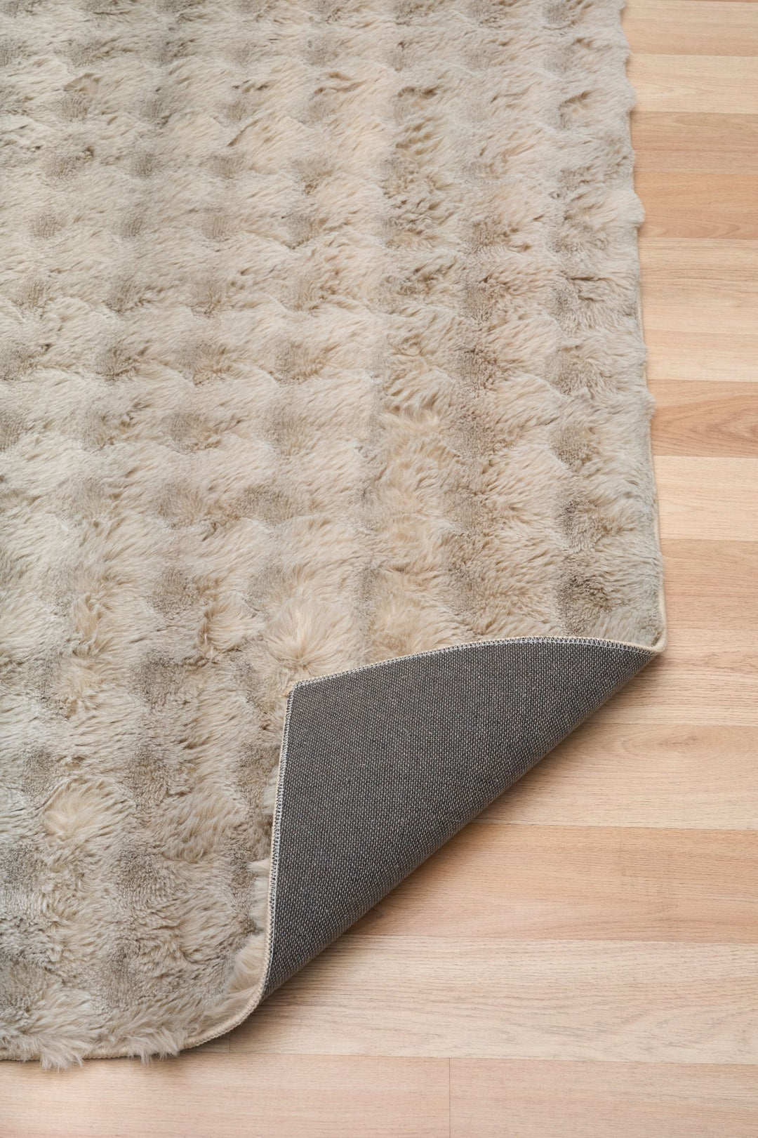 Light beige textured rug in living room with brown leather sofa, pillows, and round wooden side table.