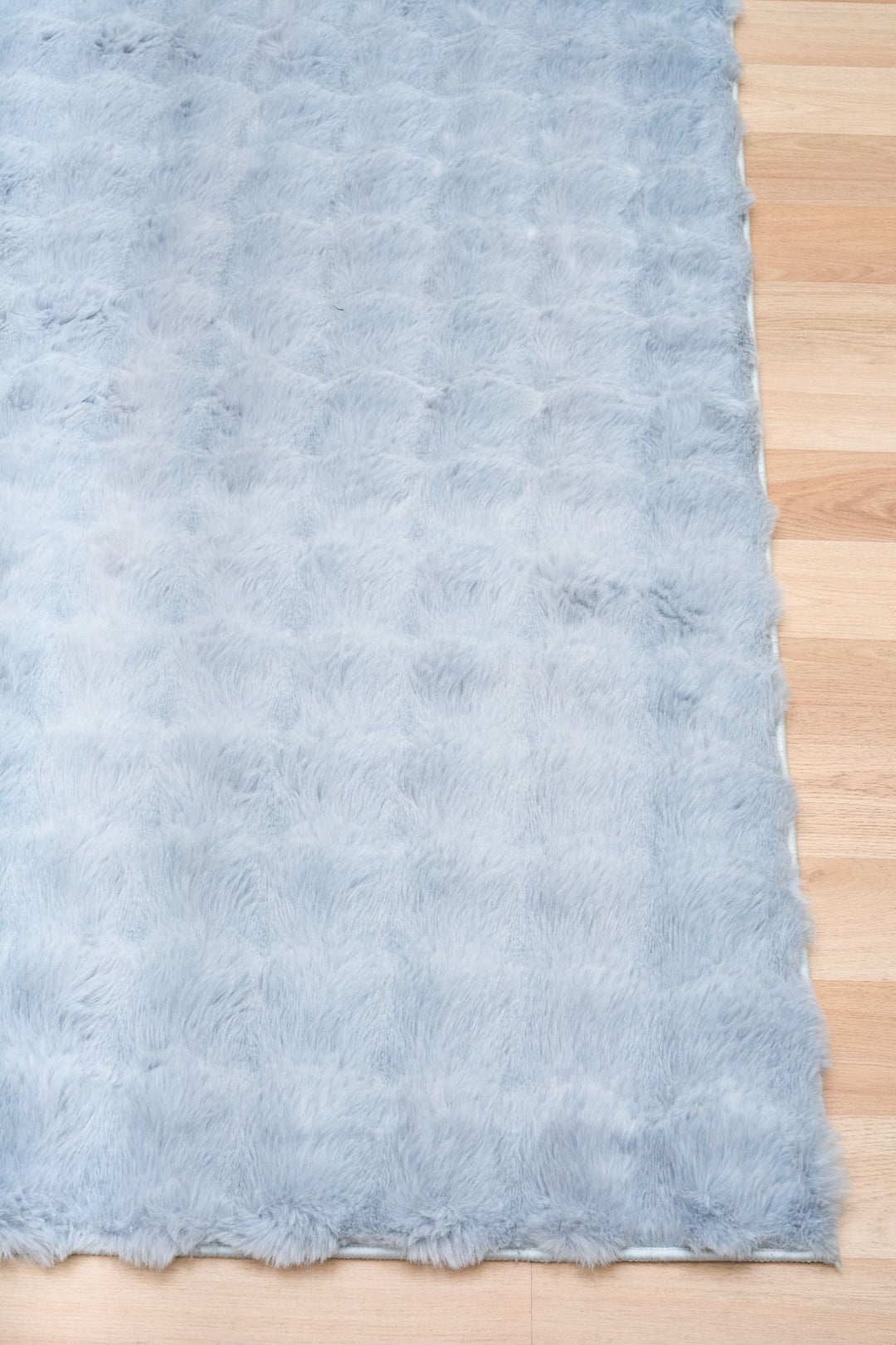 Light blue fluffy rug corner on wooden floor.