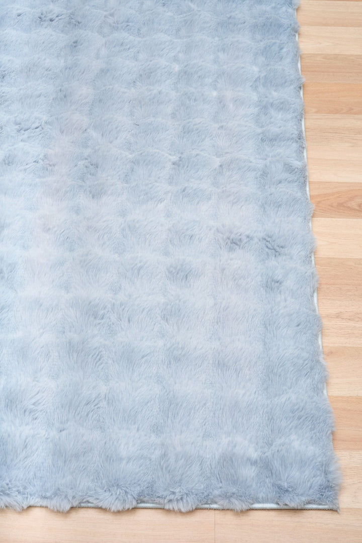 Light blue fluffy rug corner on wooden floor.