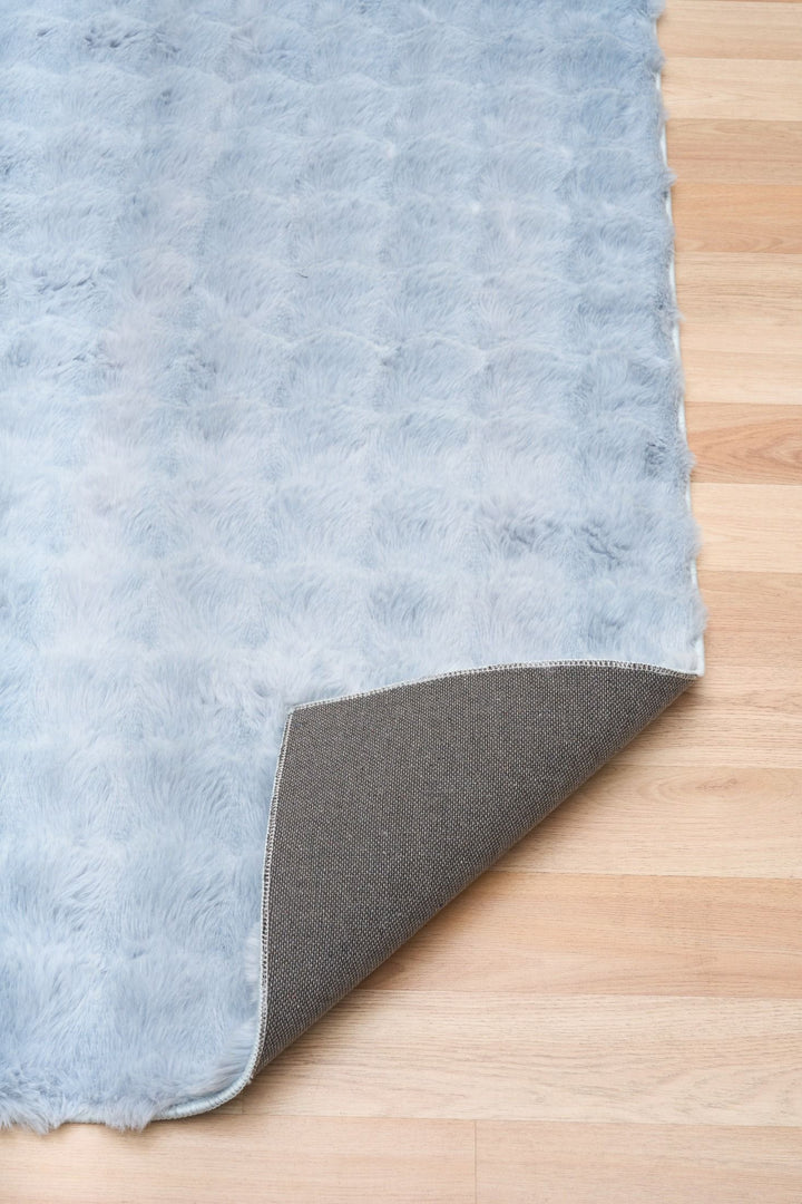 Close-up of light blue textured rug with corner flipped to show non-slip backing.