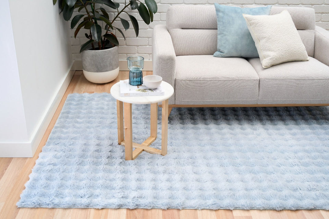 Light blue textured rug in modern living room with beige sofa, pillows, and side table.