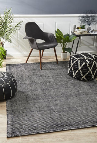 A modern black cotton and rayon rug with a geometric pattern, displayed in a room with a gray chair and decorative items.