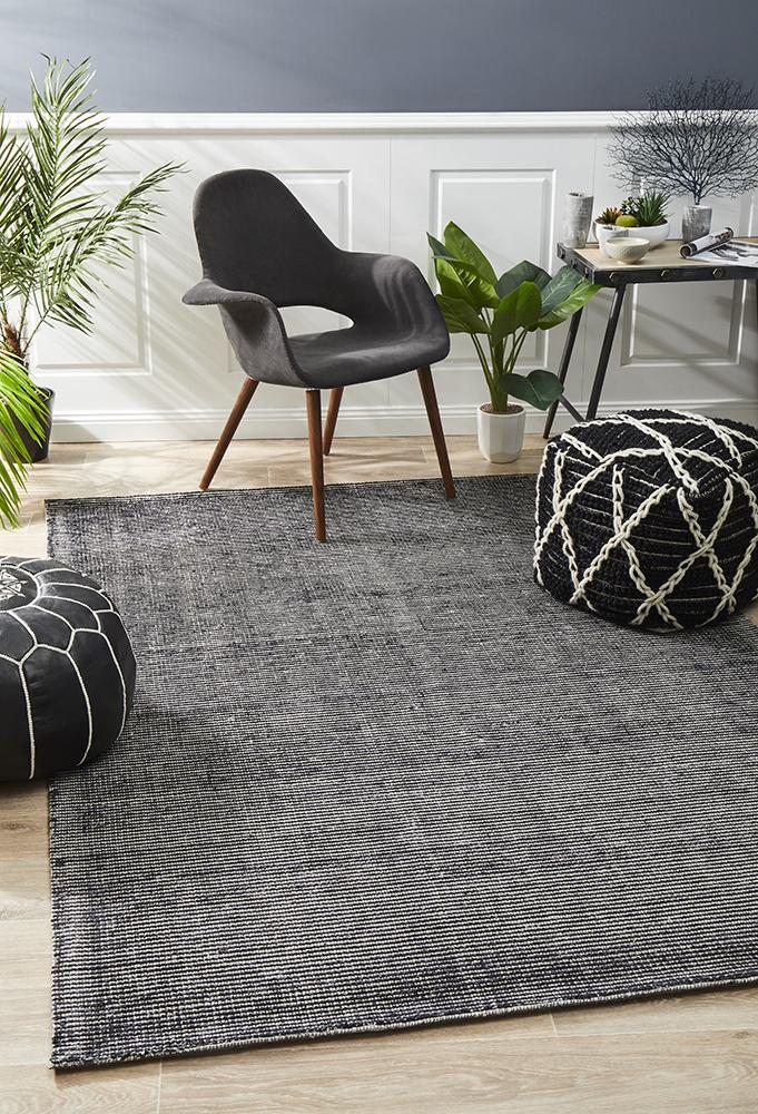A modern black cotton and rayon rug with a geometric pattern, displayed in a room with a gray chair and decorative items.