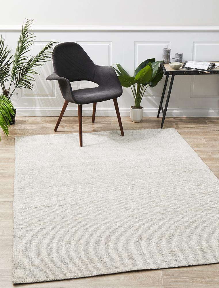 An ivory cotton rayon rug with a modern design, featuring a low pile and rectangular shape, displayed in a room with a black chair and green plant.