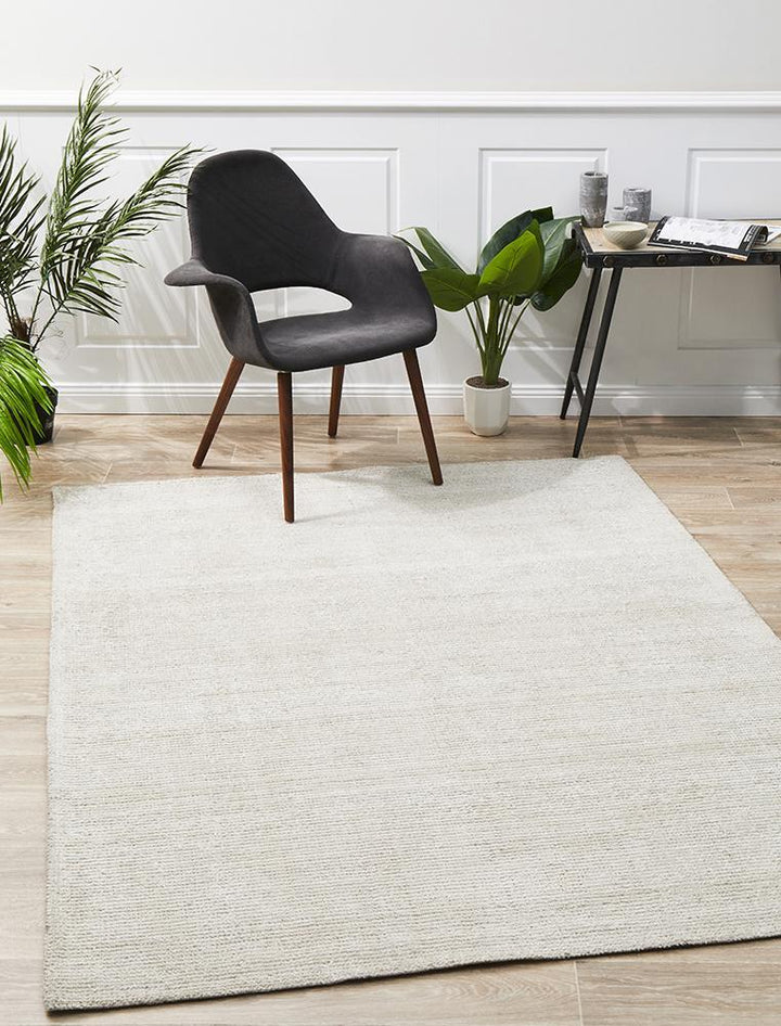 An ivory cotton rayon rug with a modern design, featuring a low pile and rectangular shape, displayed in a room with a black chair and green plant.