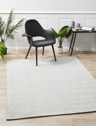 A modern rectangular rug with a sky blue color, featuring a contemporary design and made of a blend of rayon and cotton. A black chair and wooden floor accentuate the rug's aesthetic appeal.